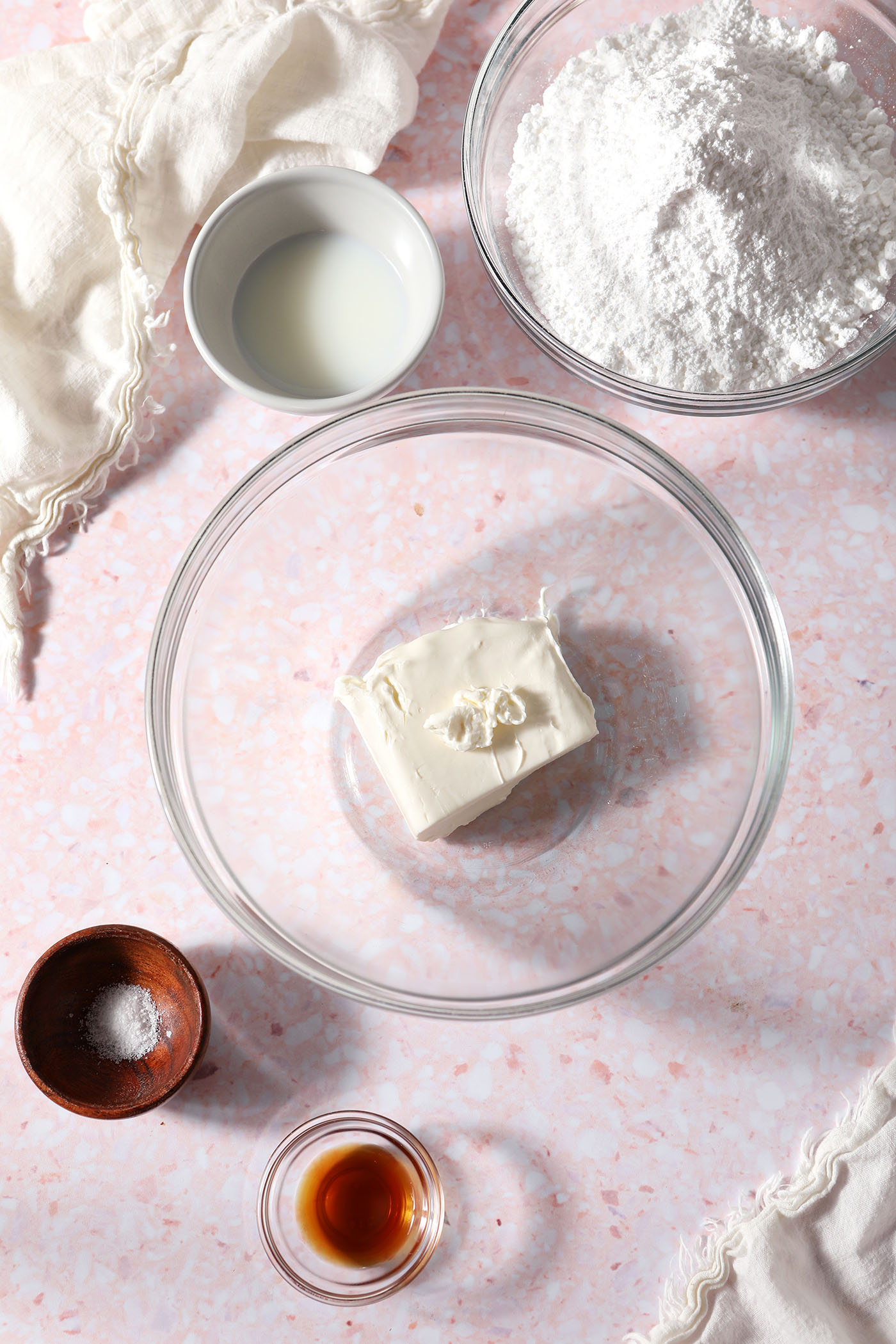 Ingredients to make cream cheese icing in bowls on a pink surface