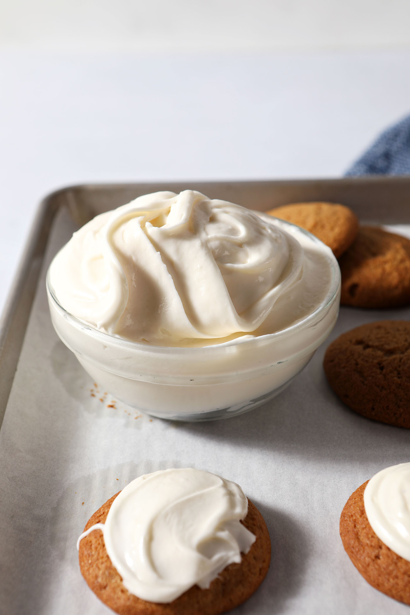 Creamy cream cheese icing in a bowl next to pumpkin cookies on a sheet pan