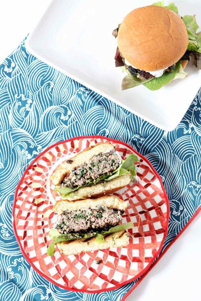 A halved Spinach and Feta Burger sits on a patterned red plate while another sits on a white platter