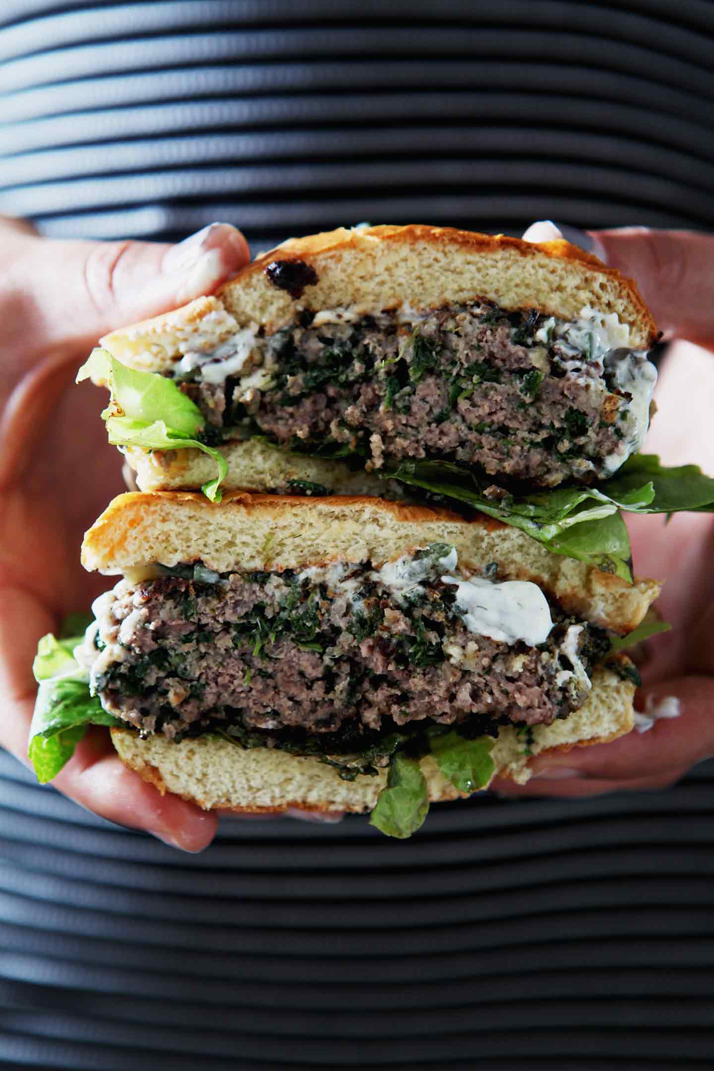 A woman holds a halved Greek Beef Burger