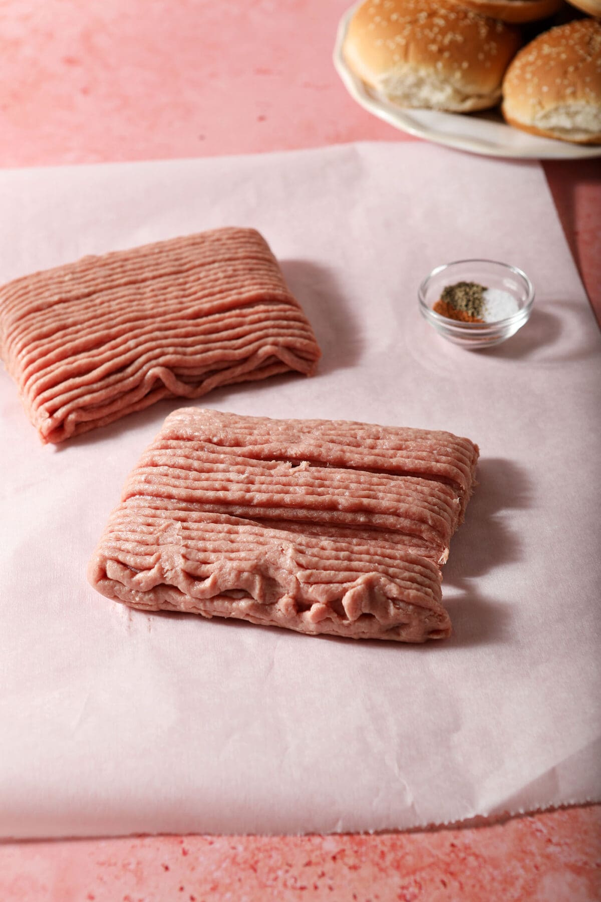 Ground turkey bricks on a sheet of parchment with a bowl of seasoning