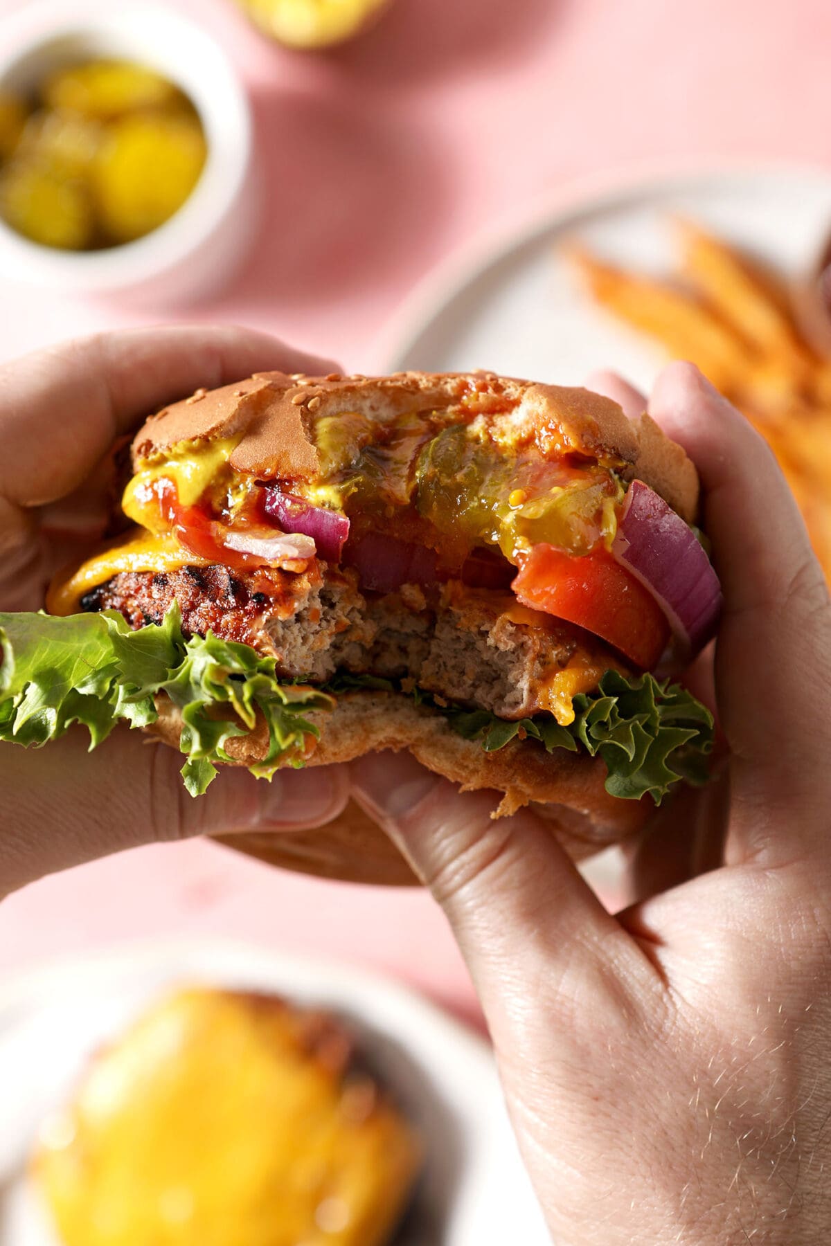 A person holds a bitten-into turkey burger above a pink surface
