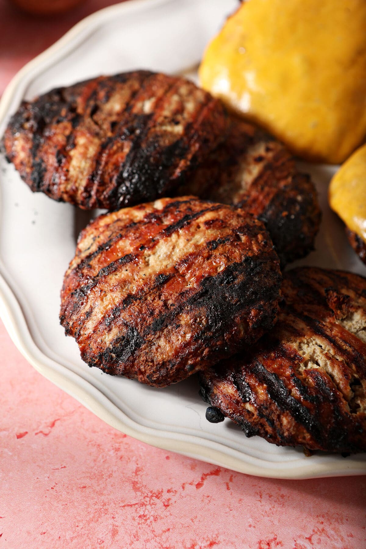 Close up of grilled turkey burgers on a white plate on a pink surface