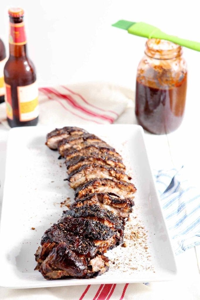 Dry rubbed Memphis Barbecue Ribs are served on a platter, shown with beer and barbecue sauce