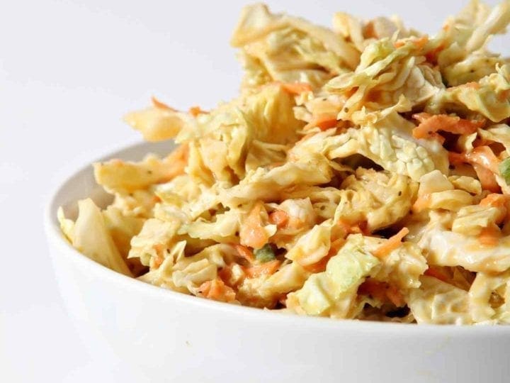 A bowl of No Mayo Honey Mustard Coleslaw sits on a white background.