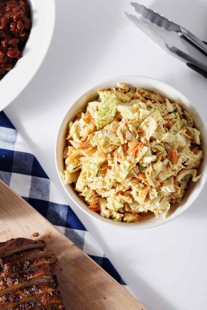 No Mayo Honey Mustard Coleslaw is served in a white bowl with other BBQ dishes