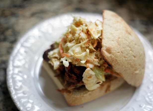 No Mayo Honey Mustard Coleslaw sits on top of a pulled pork barbecue sandwich, sitting on a white platter on a granite background