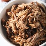 A bowl of pulled pork next to a BBQ sauce