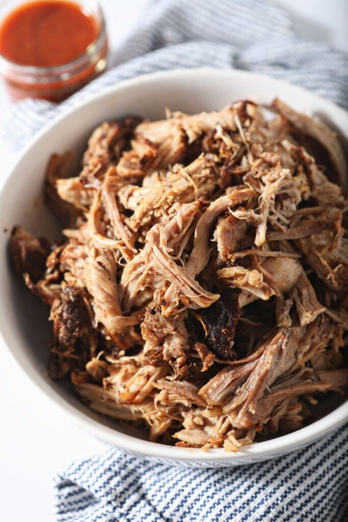 A bowl of pulled pork next to a BBQ sauce