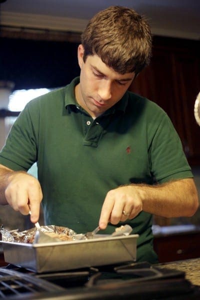 A man shreds Pulled Pork Shoulder in a metal baking dish on a stovetop