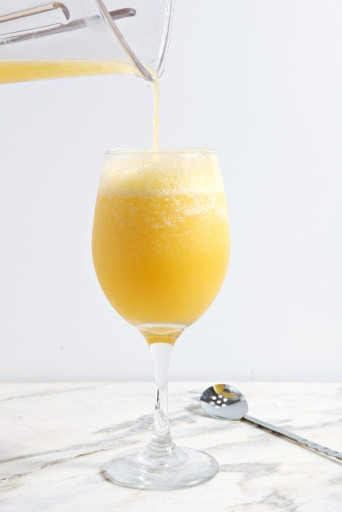 Pitcher of orange juice pouring into glass of mimosa 