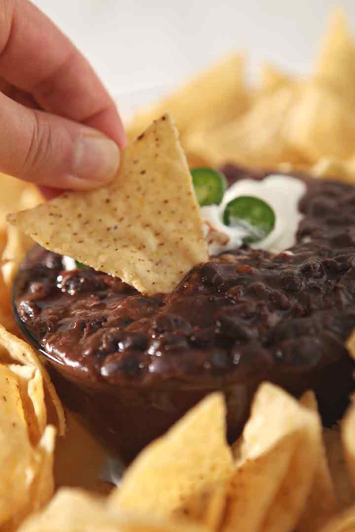 A woman dips a tortilla into Black Bean Dip, close up