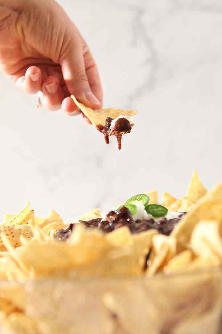 A woman lifts a tortilla covered in dip out of the bowl