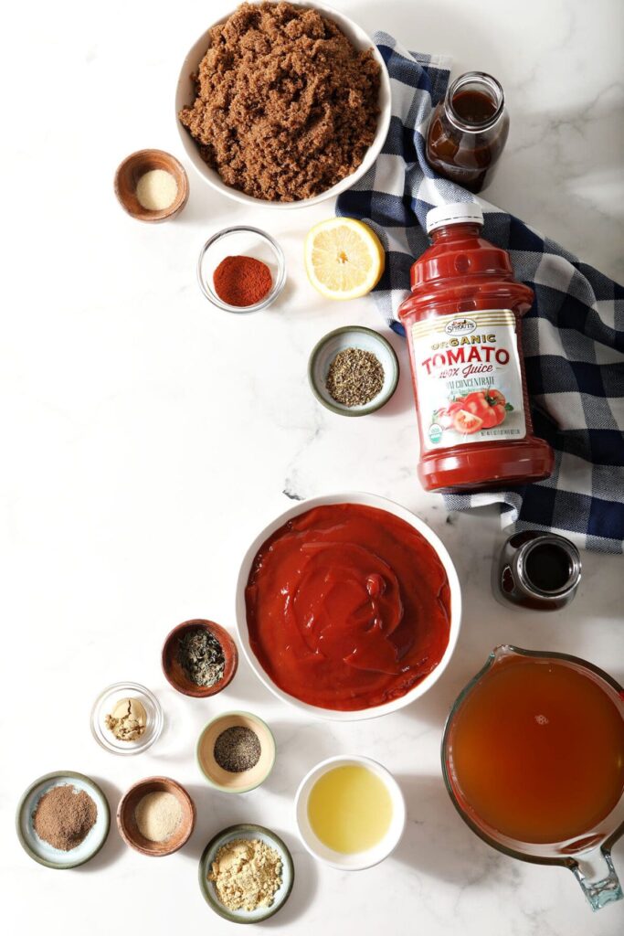 Ingredients to make homemade BBQ sauce in bowls and containers on a marble countertop with a blue buffalo check napkin