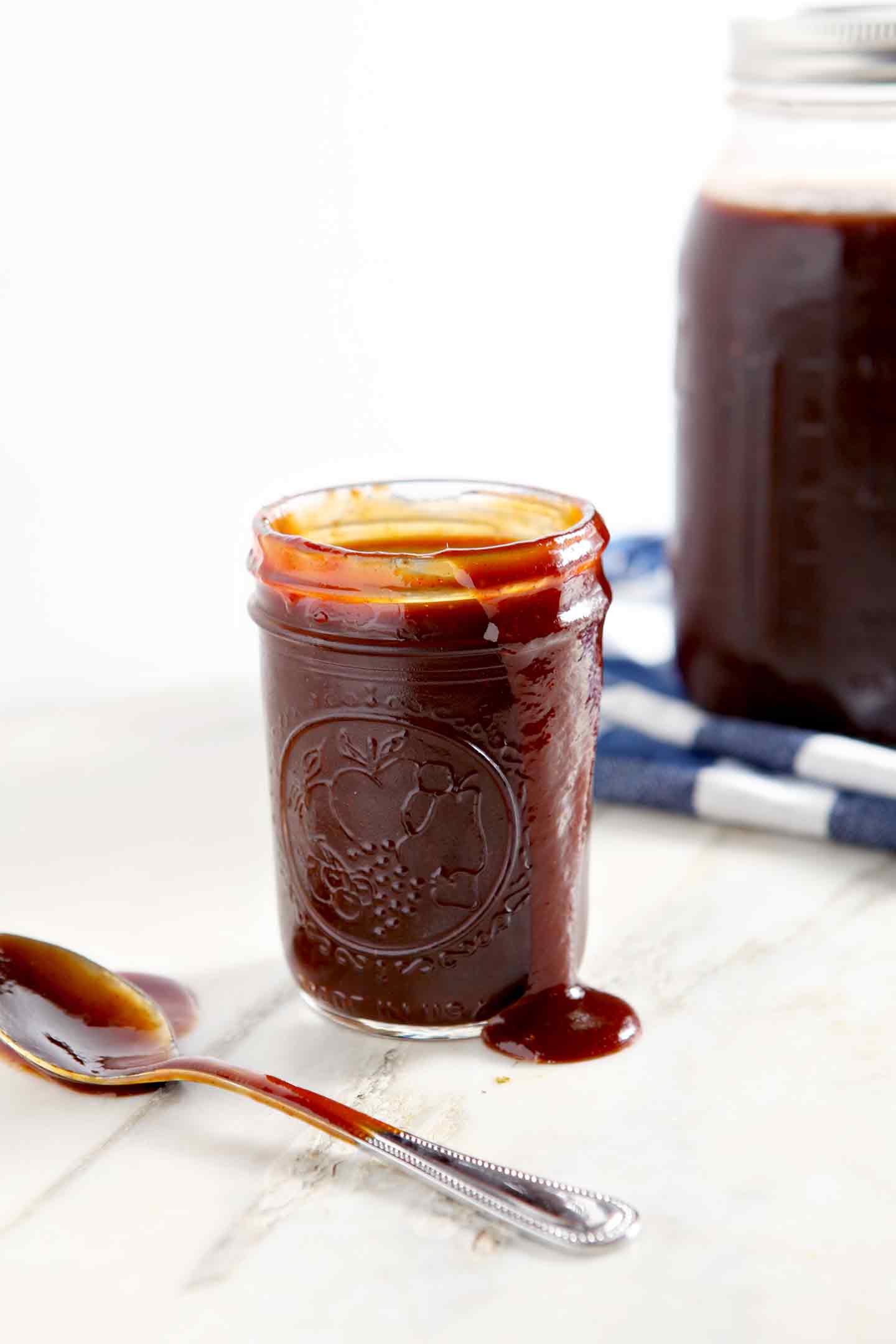 Barbecue sauce spills over the top of a jar, shown with a spoon