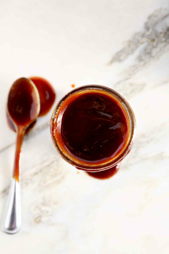 Overhead view of barbecue sauce in a glass jar next to a spoon