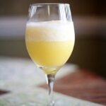 A blended mimosa in a wine glass sits on top of a wooden table with green decorative placemats