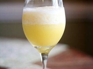 A blended mimosa in a wine glass sits on top of a wooden table with green decorative placemats