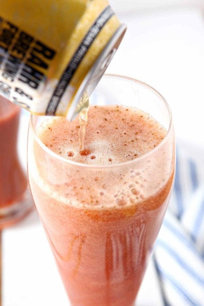 A can of beer pours into a pilsner glass full of red liquid