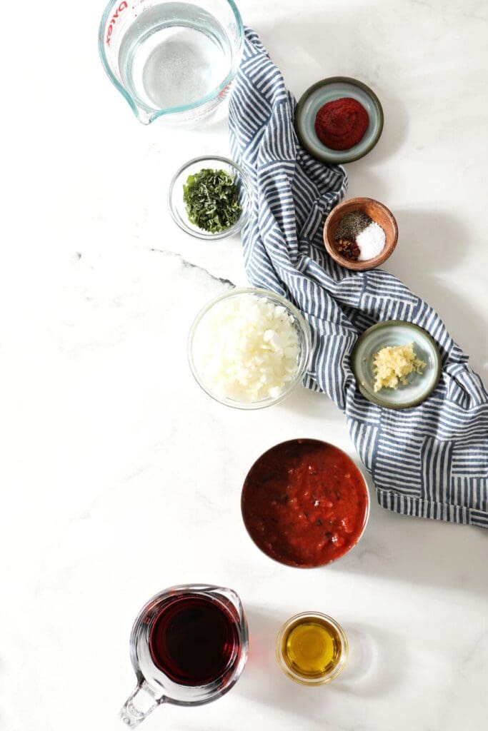 Ingredients to make easy marinara sauce on marble next to a blue checked towel