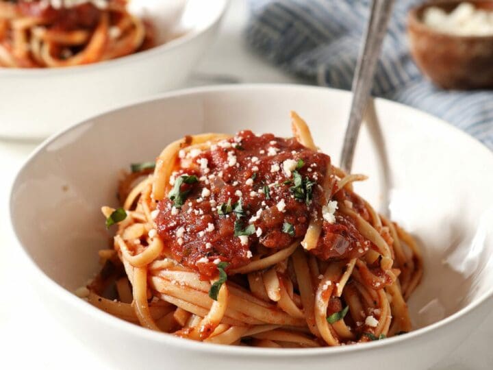 Close up of a white bowl holding spaghetti covered in marinara sauce