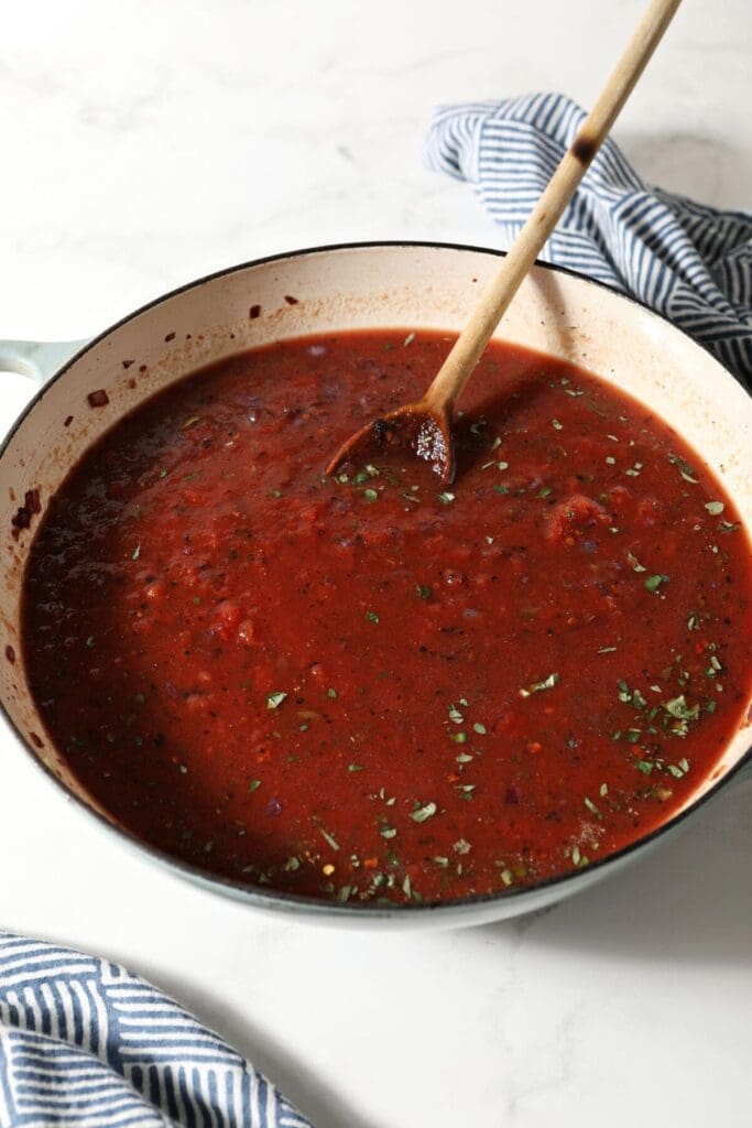 A pan full of cooked marinara sauce with a wooden spoon before serving