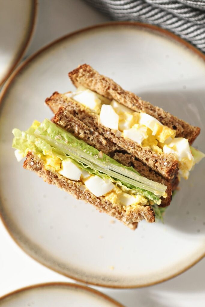 A halved egg salad sandwich on a white plate