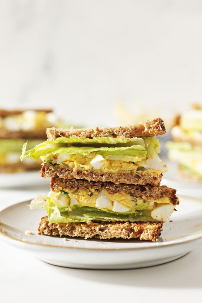 A halved egg salad sandwich with lettuce on a white plate