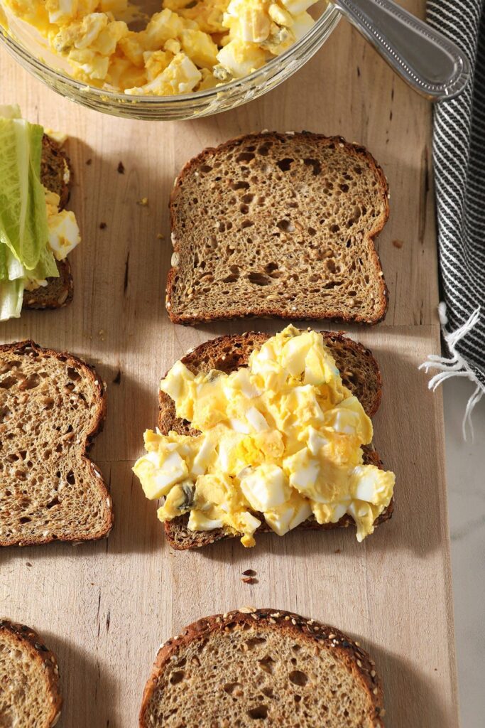 Toasted bread on a board, one topped with egg salad