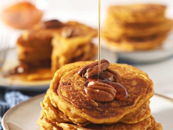 Syrup drizzles on top of a stack of Buttermilk Pumpkin Spice Pancakes with pecans on top