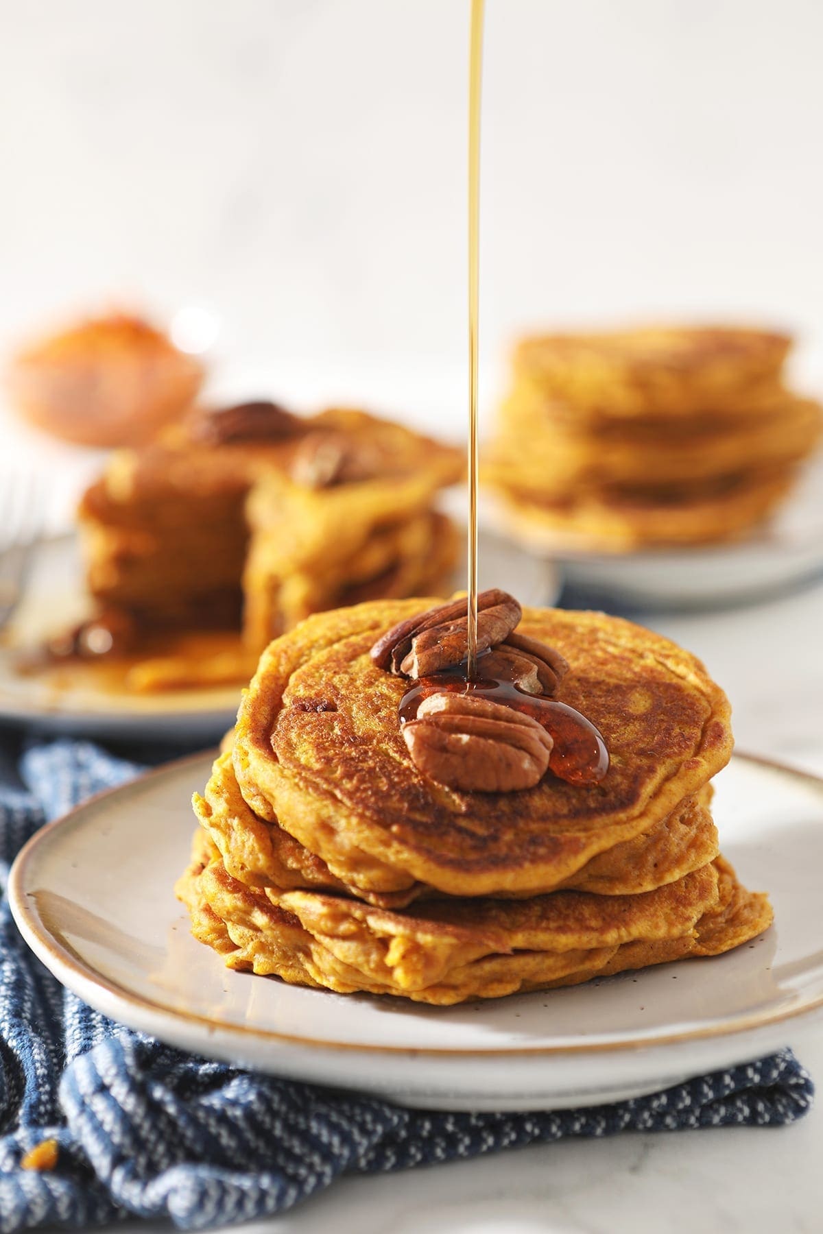 Syrup drizzles on top of a stack of Buttermilk Pumpkin Spice Pancakes with pecans on top