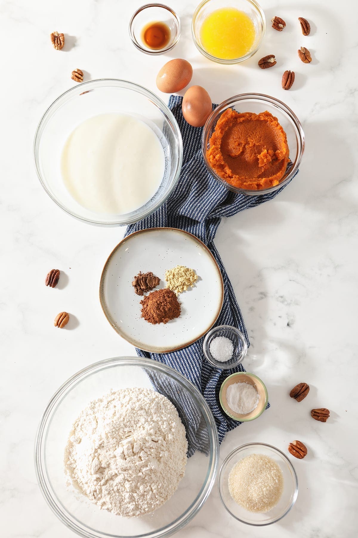 Pancake ingredients in bowls on a marble background with a blue striped towel