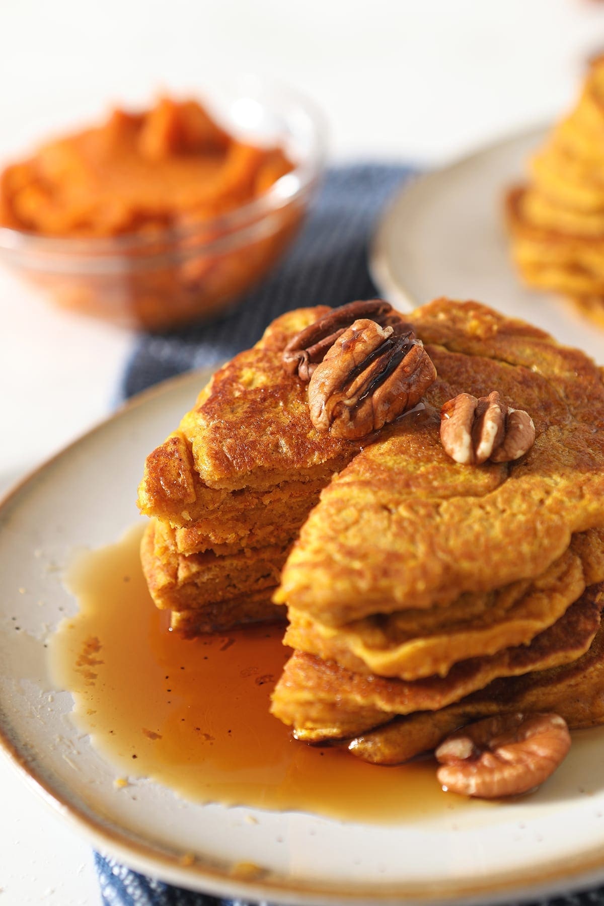 Close up of a stack of Buttermilk Pumpkin Spice Pancakes missing a triangular bite with syrup and pecans 