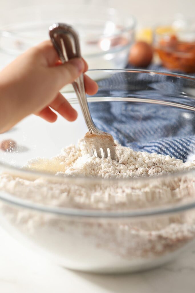 A girl stirs the pancake dry ingredients with a fork