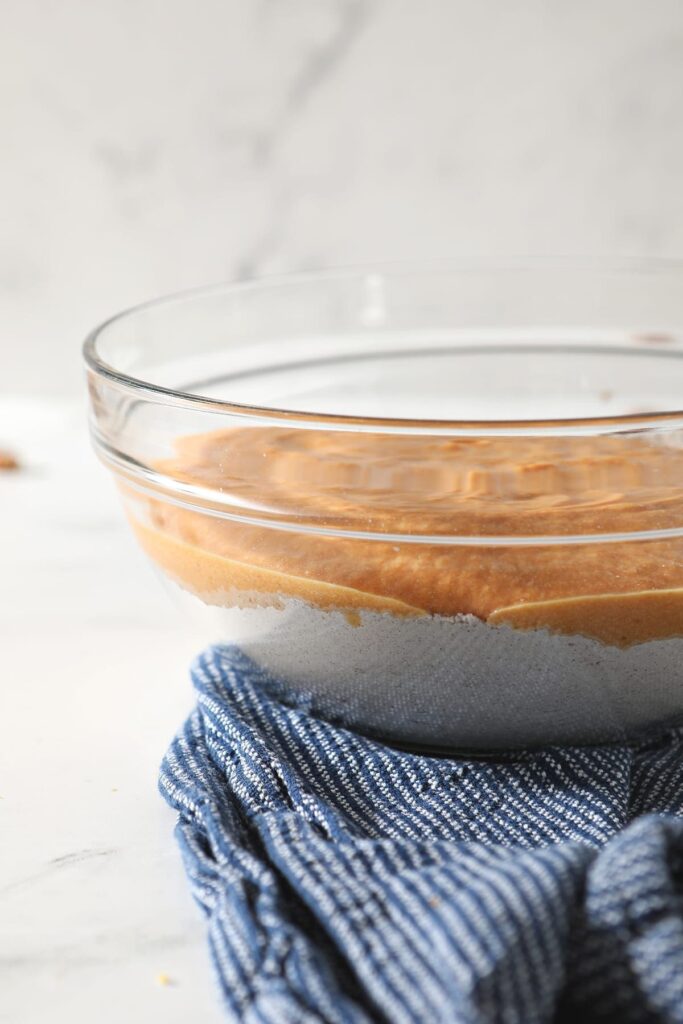 The side of a glass bowl holding a layer of dry ingredients and the wet ingredients on top, before mixing