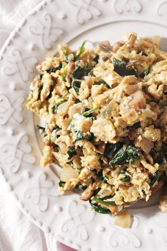 Close up of a serving of Scrambled Eggs with Spinach, mushrooms and onions on a white plate