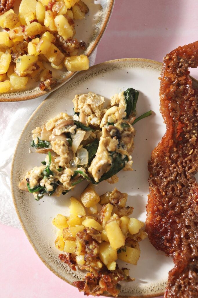 A serving of veggie scrambled eggs on a plate next to home fries and candied bacon