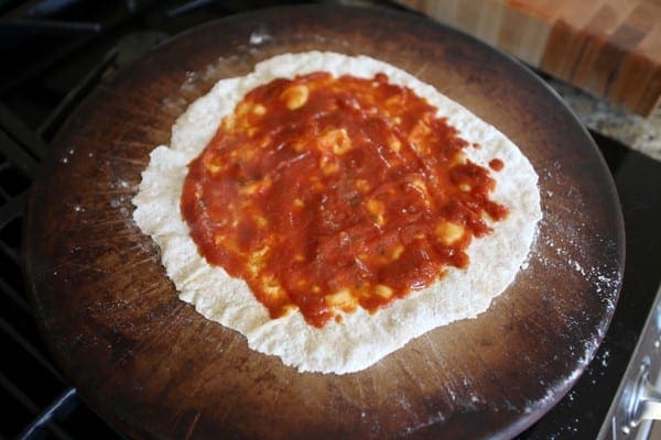 A close up of sauce on dough on a pizza stone 