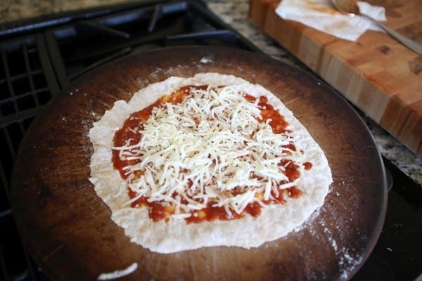 Shredded cheese and sauce on dough on pizza stone 