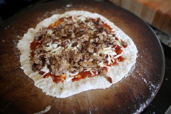 Close up of meat, cheese and sauce on dough on pizza stone 