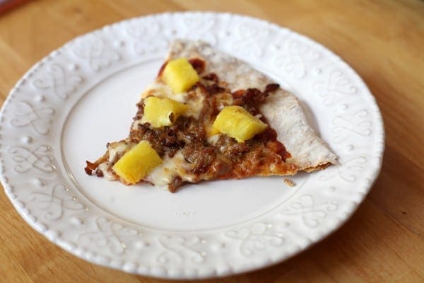 A slice of pork and pineapple pizza on white plate
