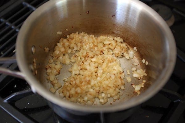 Chopped onions and garlic cook in a metal pot on the gas stovetop