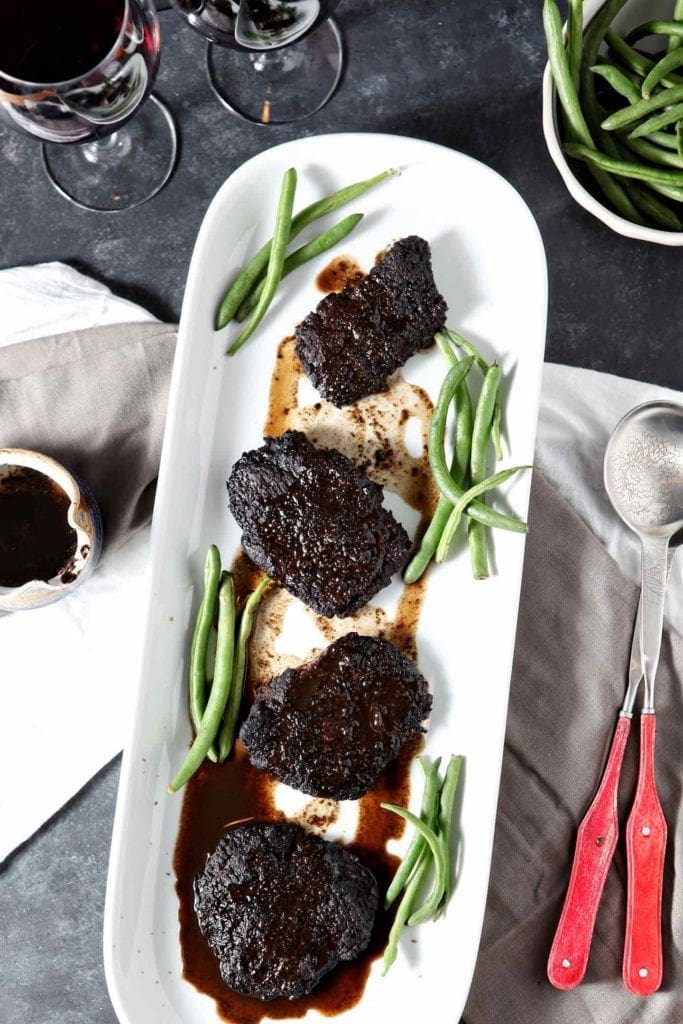 A platter of Baked Steak sits on a tablescape, served with green beans