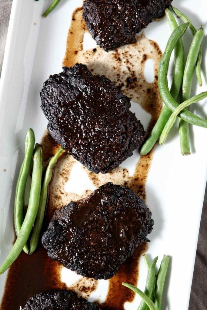 baked steak on a white plate with green beans