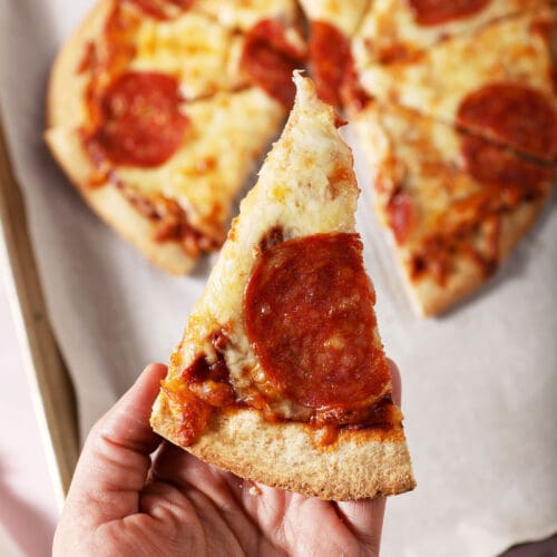 A hand holds a slice of homemade pepperoni pizza