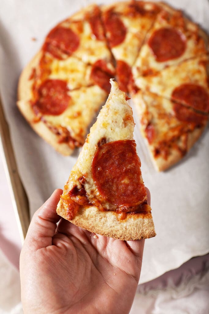 A hand holds a slice of homemade pepperoni pizza