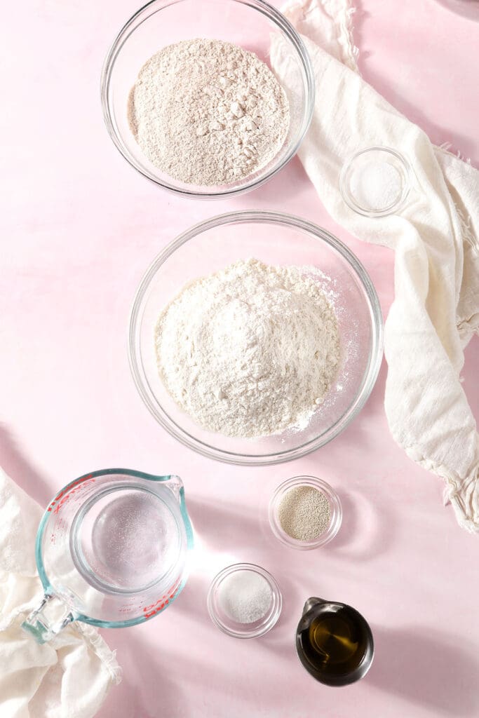 Ingredients to make homemade pizza dough in bowls on a pink surface