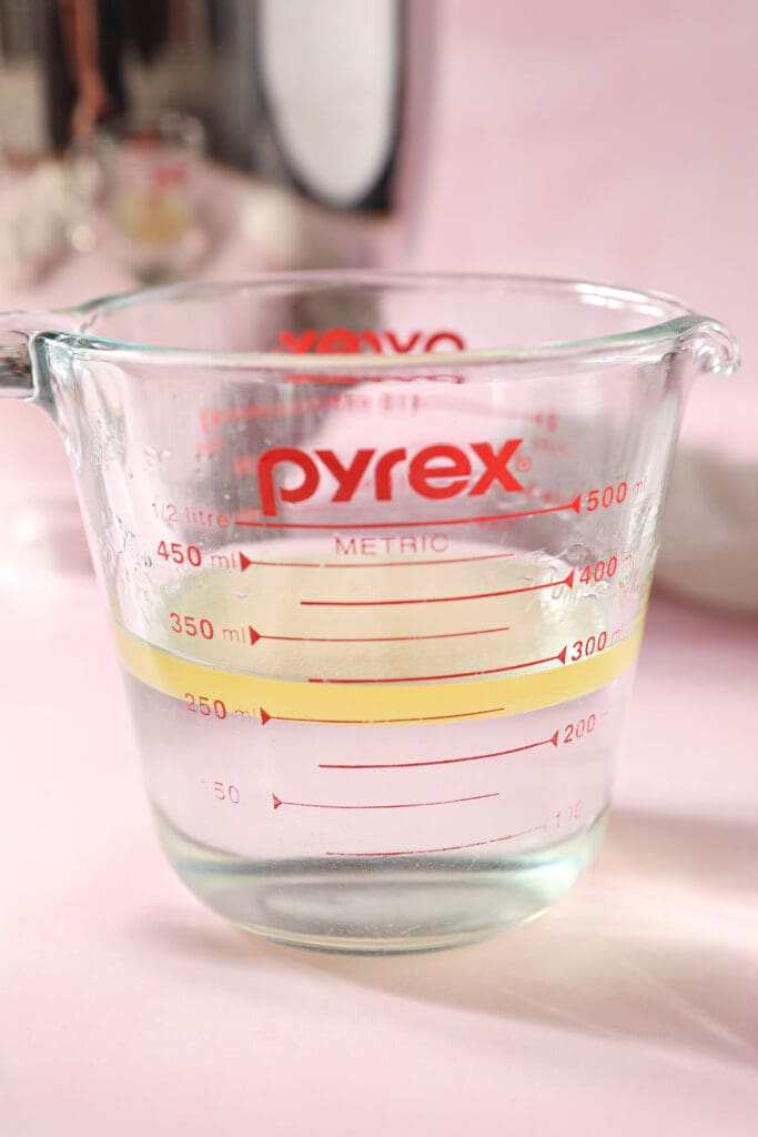 A liquid measuring cup of water, oil and sugar on a pink surface