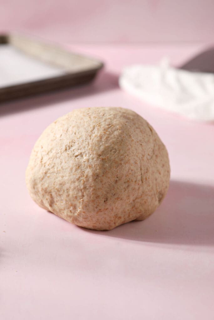 A round of pizza dough on a pink surface