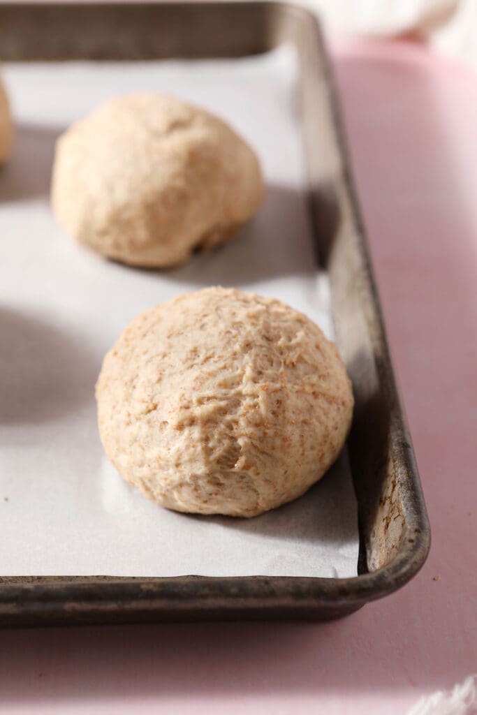 Four rounds of pizza dough before rising on a parchment-lined sheet pan